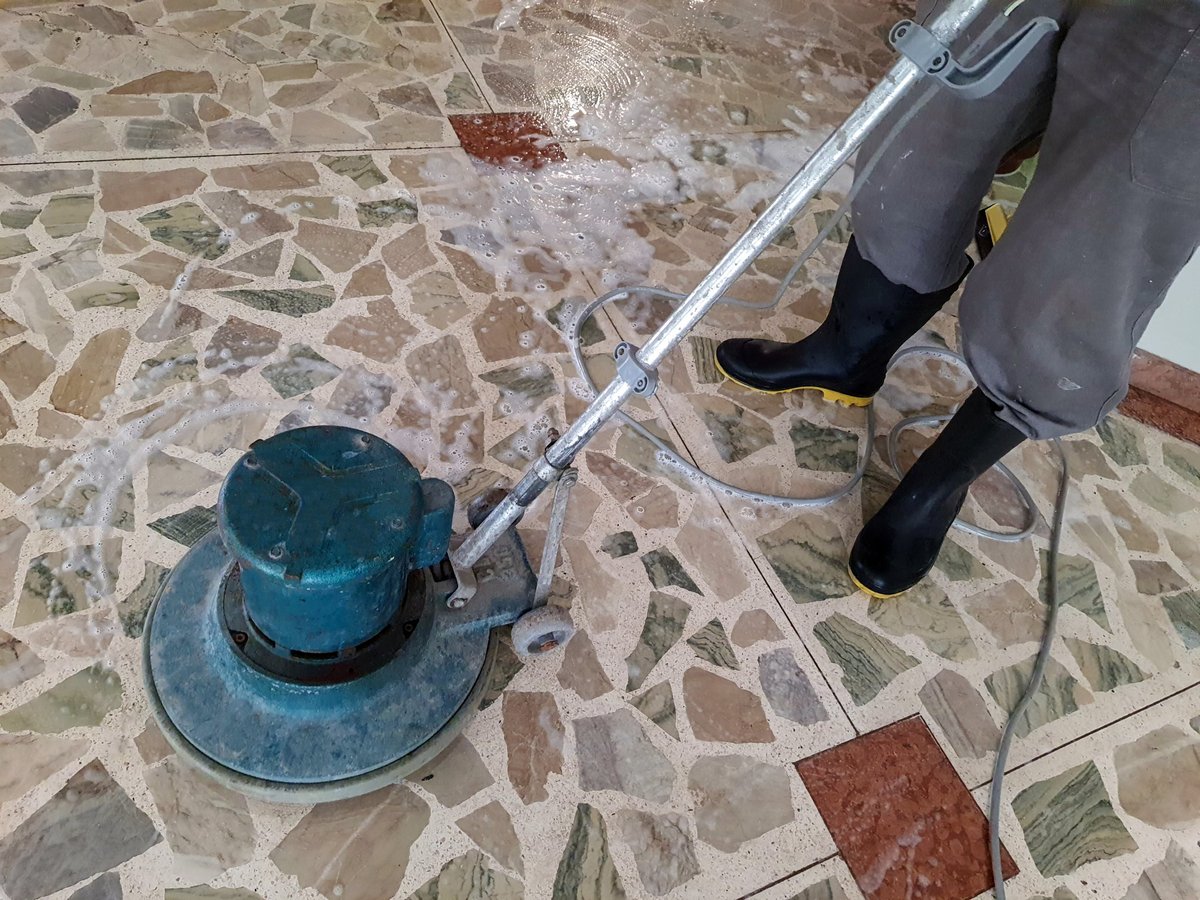 Man in rubber boots washing the floor with an industrial floor polisher